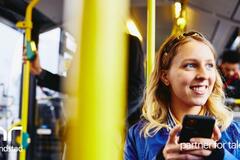 Mujer sonriente, mirando al exterior mientras sostiene su teléfono y está sentada en el autobús.