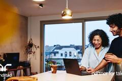 Una mujer y un hombre de pie junto a la encimera de la cocina, mirando una computadora portátil. Están sonriendo.