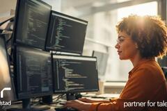  Mujer sentada en un escritorio mirando cuatro pantallas de computadora con código. Generado por IA.