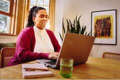 mujer sentada en una mesa escribiendo en su laptop.