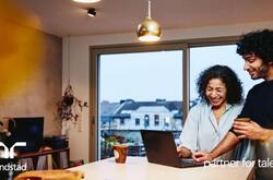 Una mujer y un hombre de pie junto a la encimera de la cocina, mirando una computadora portátil. Están sonriendo.