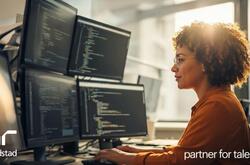  Mujer sentada en un escritorio mirando cuatro pantallas de computadora con código. Generado por IA.