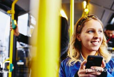 Mujer sonriente, mirando al exterior mientras sostiene su teléfono y está sentada en el autobús.