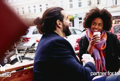 Hombre y mujer sonrientes con bebidas sentados en un banco al aire libre, conversando.