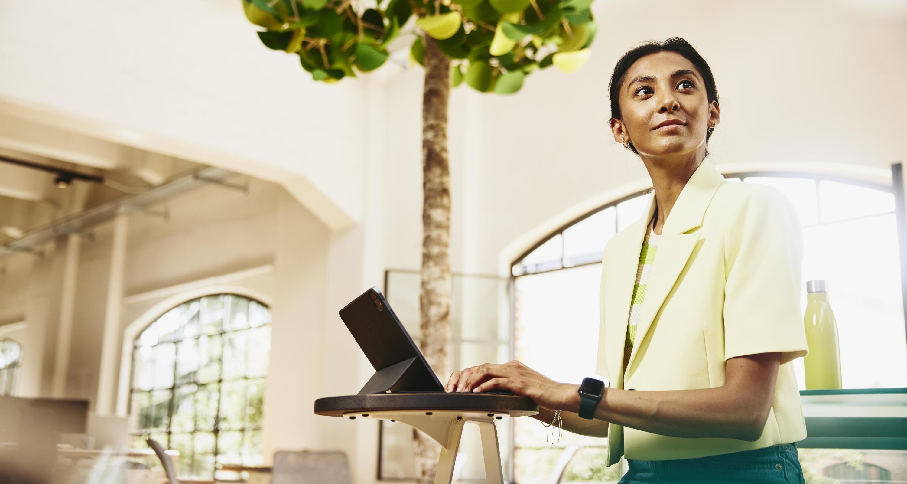 Woman looking away while sitting at table working on a tablet.